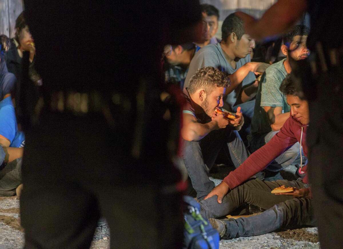An apparently undocumented immigrant eats a slice of donated pits as he sits on the ground Tuesday night, June 12, 2018 with other apparently undocumented immigrants after they were found in the back of an 18-wheel truck near loop 410 and Broadway.