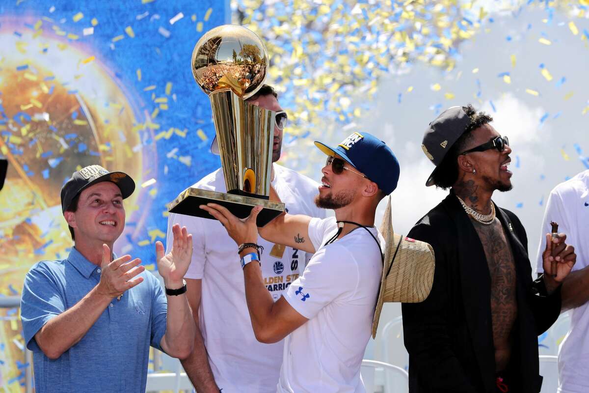 The Golden State Warriors' Stephen Curry holds up the Larry O'Brien NBA Championship Trophy as majorty owner Joe Lacob applauds at the end of the team's championship rally in downtown Oakland, Calif., on Tuesday, June 12, 2018. (Ray Chavez/Bay Area News Group/TNS)