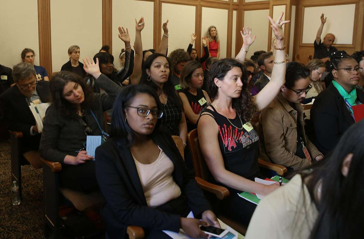 The public show silent opinion by raising hands during a hearing held by San Francisco supervisor Sandra Fewer about the city's controversial gang injunction program at city hall on Wednesday, June 13, 2018 in San Francisco, Calif.