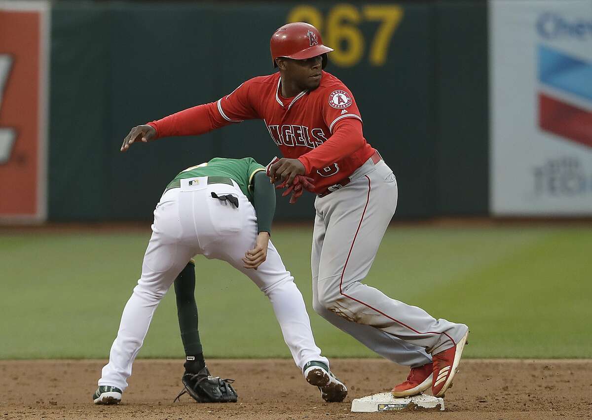 Los Angeles Angels' Justin Upton, top, runs toward third base after Oakland Athletics second baseman Jed Lowrie, bottom, could not field a throwing error by third baseman Chad Pinder during the third inning of a baseball game in Oakland, Calif., Friday, June 15, 2018. (AP Photo/Jeff Chiu)