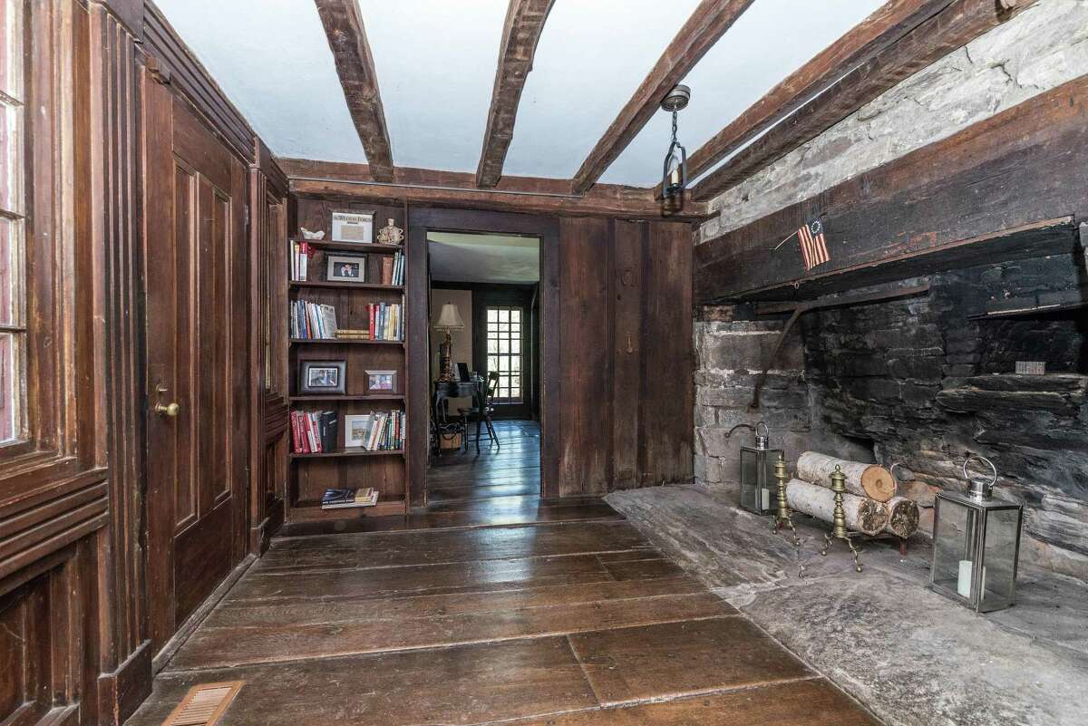 The foyer has hand-hewn exposed beams on the ceiling and walls, built-in bookshelves, and a fireplace with an oven that looks original to the house.