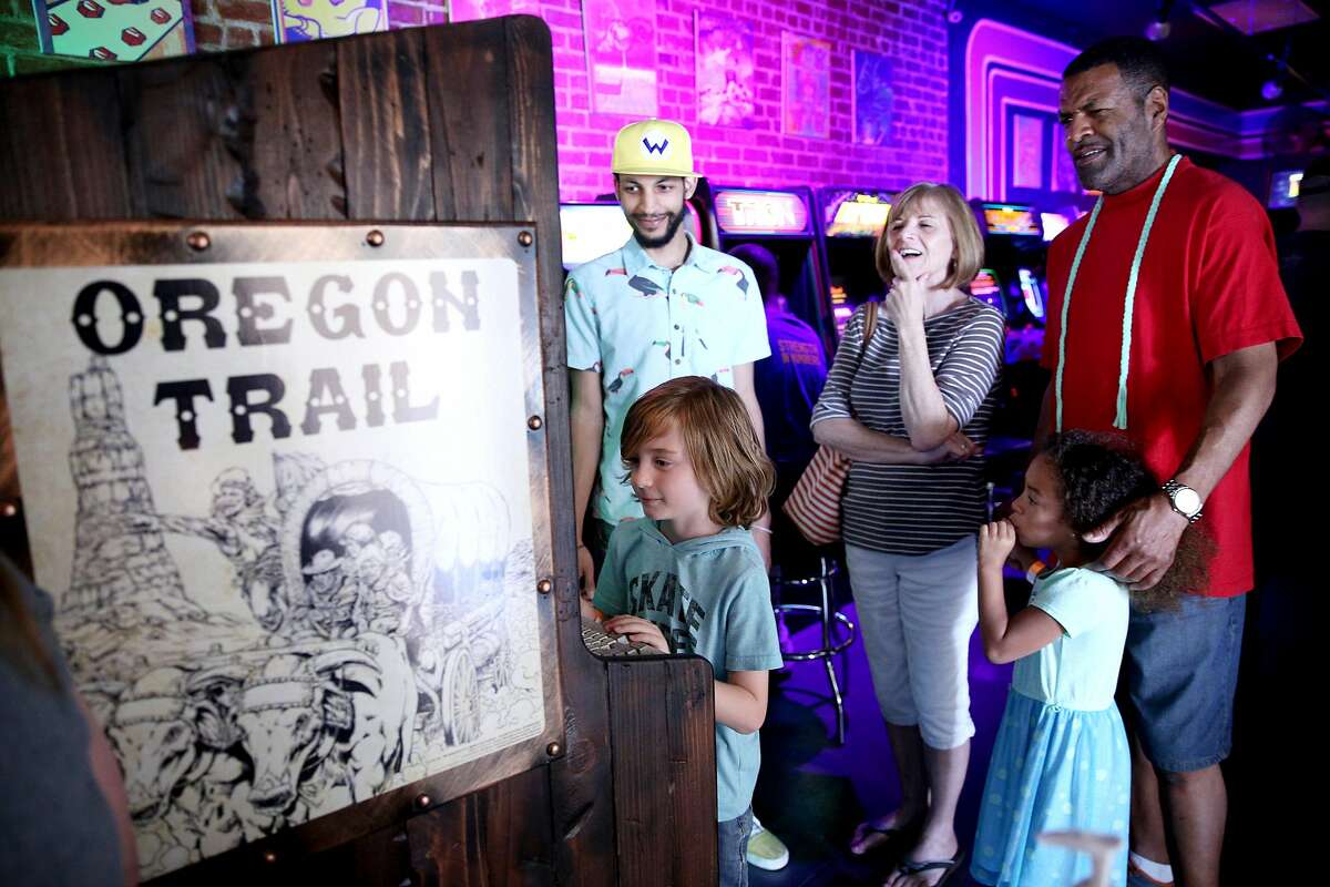From left: Sebastian Gross, 7, plays the Oregon Trail game as Jonathan Williams, Joanne Gross, Annleah Moore, 6, and Robert Moore watch and wait for a turn at High Scores Arcade, Saturday, June 16, 2018, in Hayward, Calif.