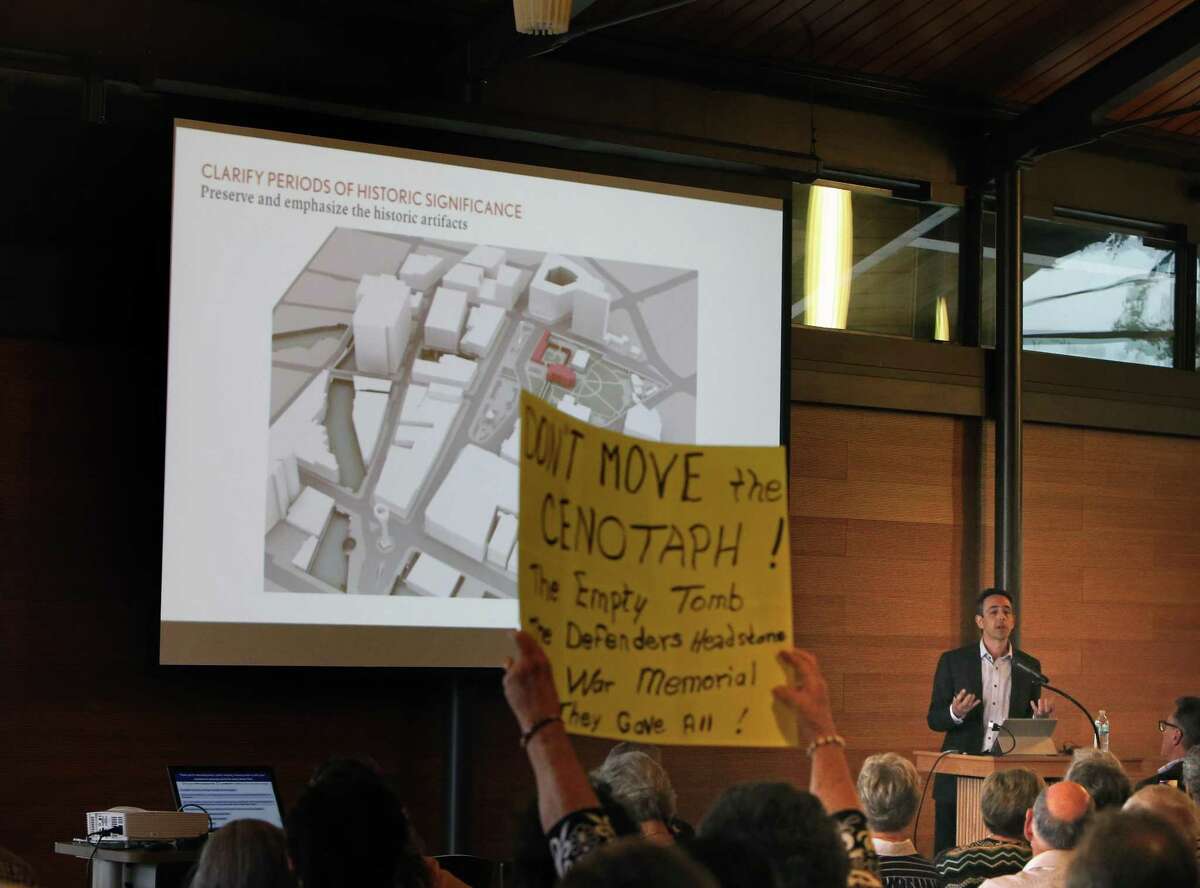 During a presentation by Eric Kramer, people begin to put up signs but were asked by some in the audience to put them down and to give him a chance to speak.