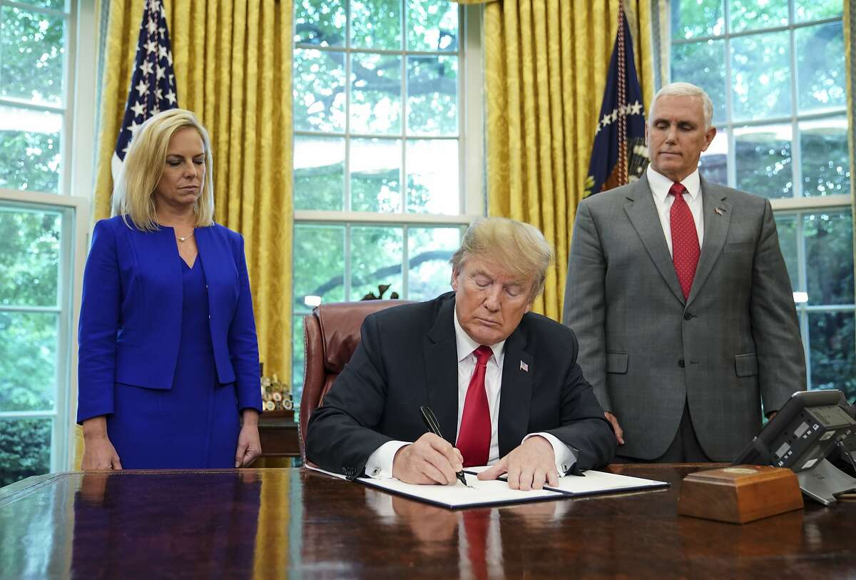 TOPSHOT - Watched by Homeland Security Secretary Kirstjen Nielsen (L) and Vice President Mike Pence, US President Donald Trump signs an executive order on immigration in the Oval Office of the White House on June 20, 2018 in Washington, DC. US President Donald Trump on Wednesday signed an executive order aimed at putting an end to the controversial separation of migrant families at the border, reversing a harsh practice that had earned international scorn."It's about keeping families together," Trump said at the signing ceremony. "I did not like the sight of families being separated," he added. 