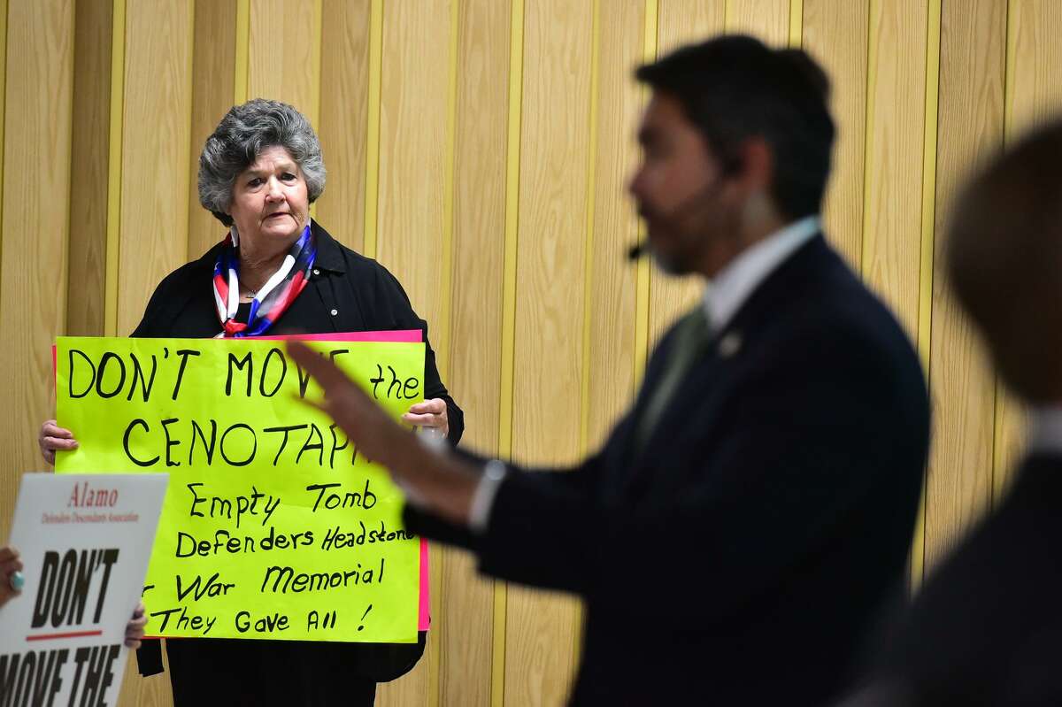 Maggie Clopton Wright holds a sign with her opinio about moving the Cenotaph as Councilman Rpberto Trvino speaks during a community meeting about the proposed changes to Alamo Plaza Thursday evening at the San Antonio Garden Center.