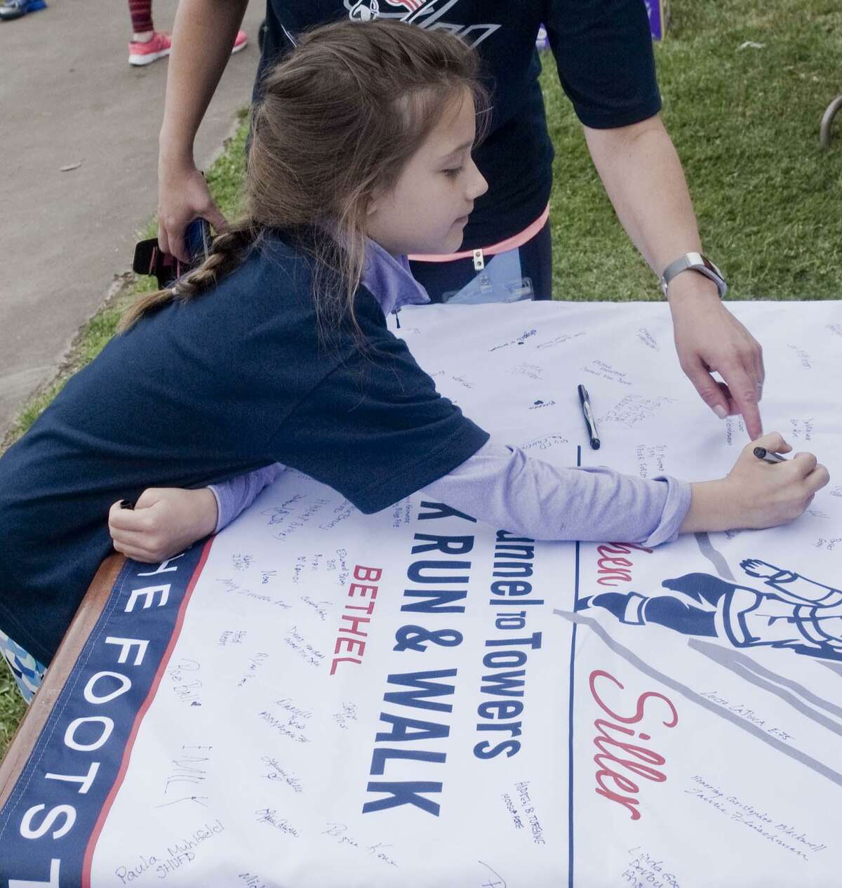 Ava Keil, 7 of Newtown, signs the Tunnel to Towers banner at Bethel High School at the inaugural 5K race honoring firefighters killed in 9/11. Sunday, June 24, 2018