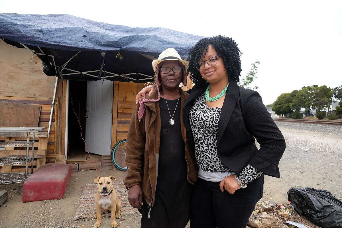 Candice Elder, 34, the founder of East Oakland Collective, stands with Elizabeth Easton, 65, in front of Easton's tiny home and her dog, Nala, at a homeless encampment in East Oakland on June 20, 2018.