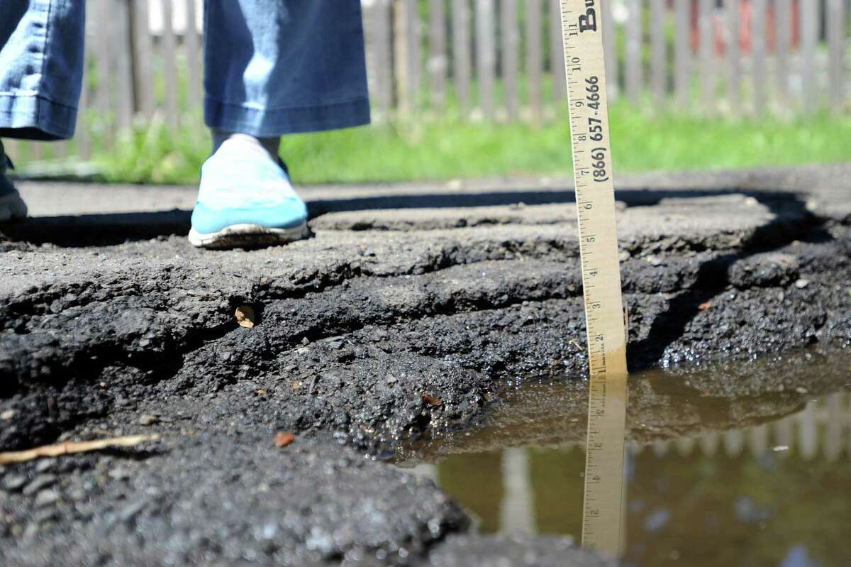 Brookside Drive resident Liberty Gilbert holds a yardstick in one of the street’s deep potholes, measuring over 5 inches from the bottom, on Tuesday in Stamford.