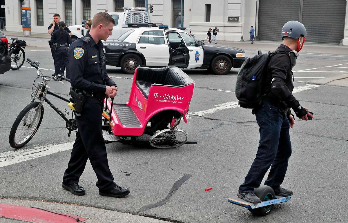 A Onewheel rider crosses by the scene of an accident after a hit and run accident involving a pedicab and vehicle on the Embarcadero in San Francisco on Wednesday, June 27, 2018.