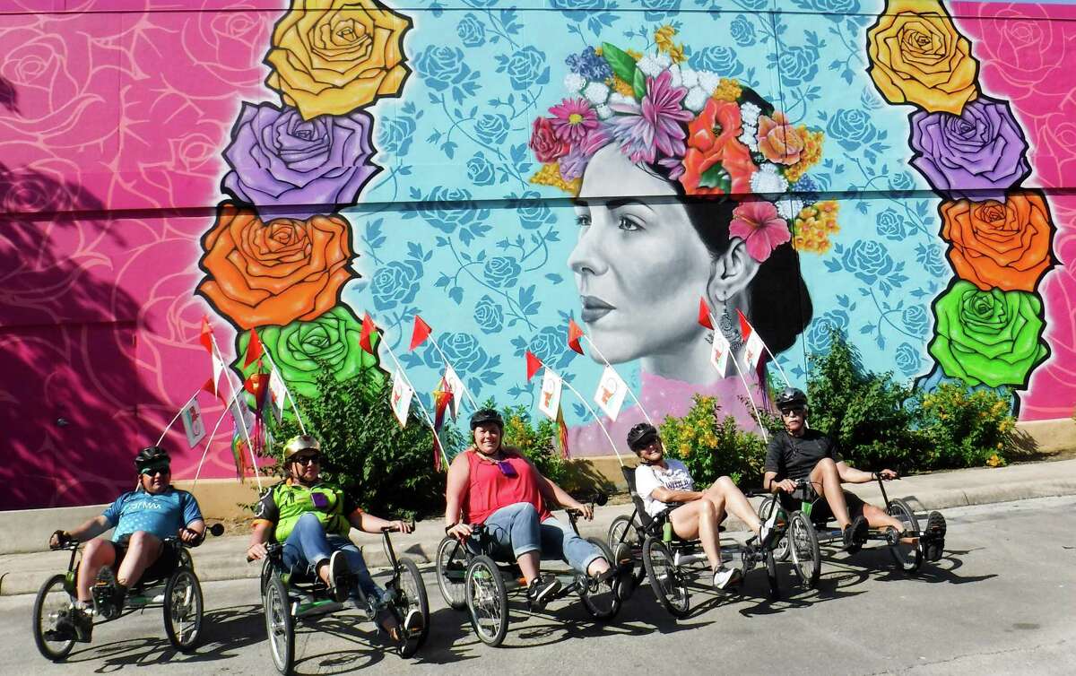 A group taking a trip guided by San Antonio Bike Tours pauses in front of a mural at the Fiesta store.