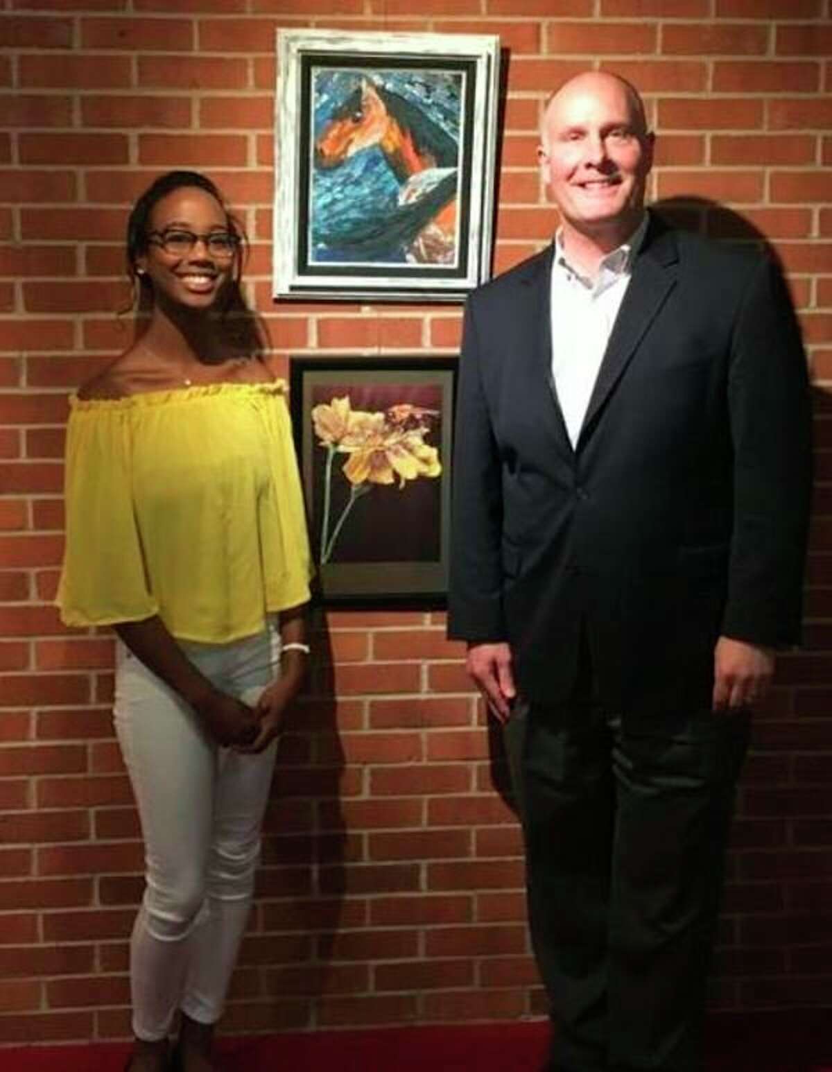 FILE — U.S. Rep. John Moolenaar congratulates Genesia Thompson on winning the Congressional Art Competition for Michigan's Fourth Congressional District during a presentation at the Midland Center for the Arts on May 2, 2018. Thompson's winning piece, 'October,' is in the center. It features marigolds and a bee.