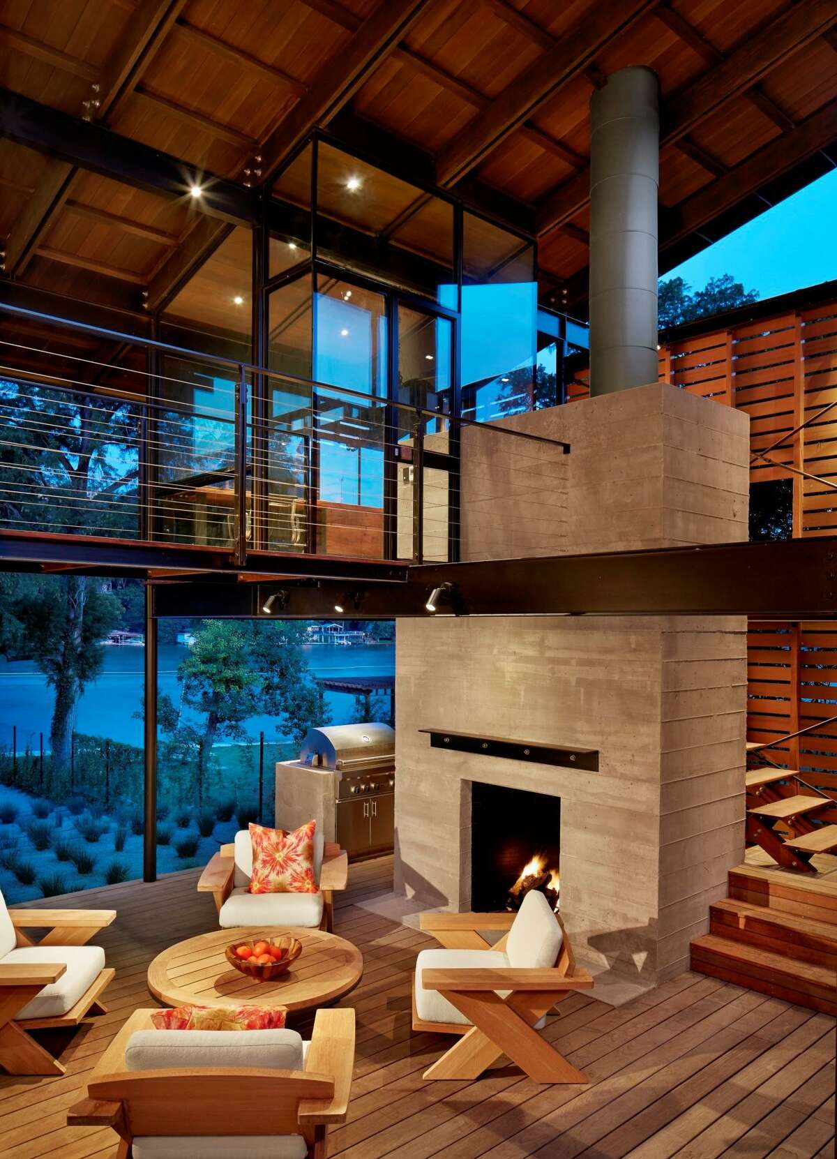 This backyard kitchen has two levels, the lower for cooking and entertaining, the upper, a glassed-in office for working with a view. The board-formed concrete fireplace is topped with a simple angled steel mantle. The lower room is open-air to catch the lake breezes and the furnishings are from Sutherland.