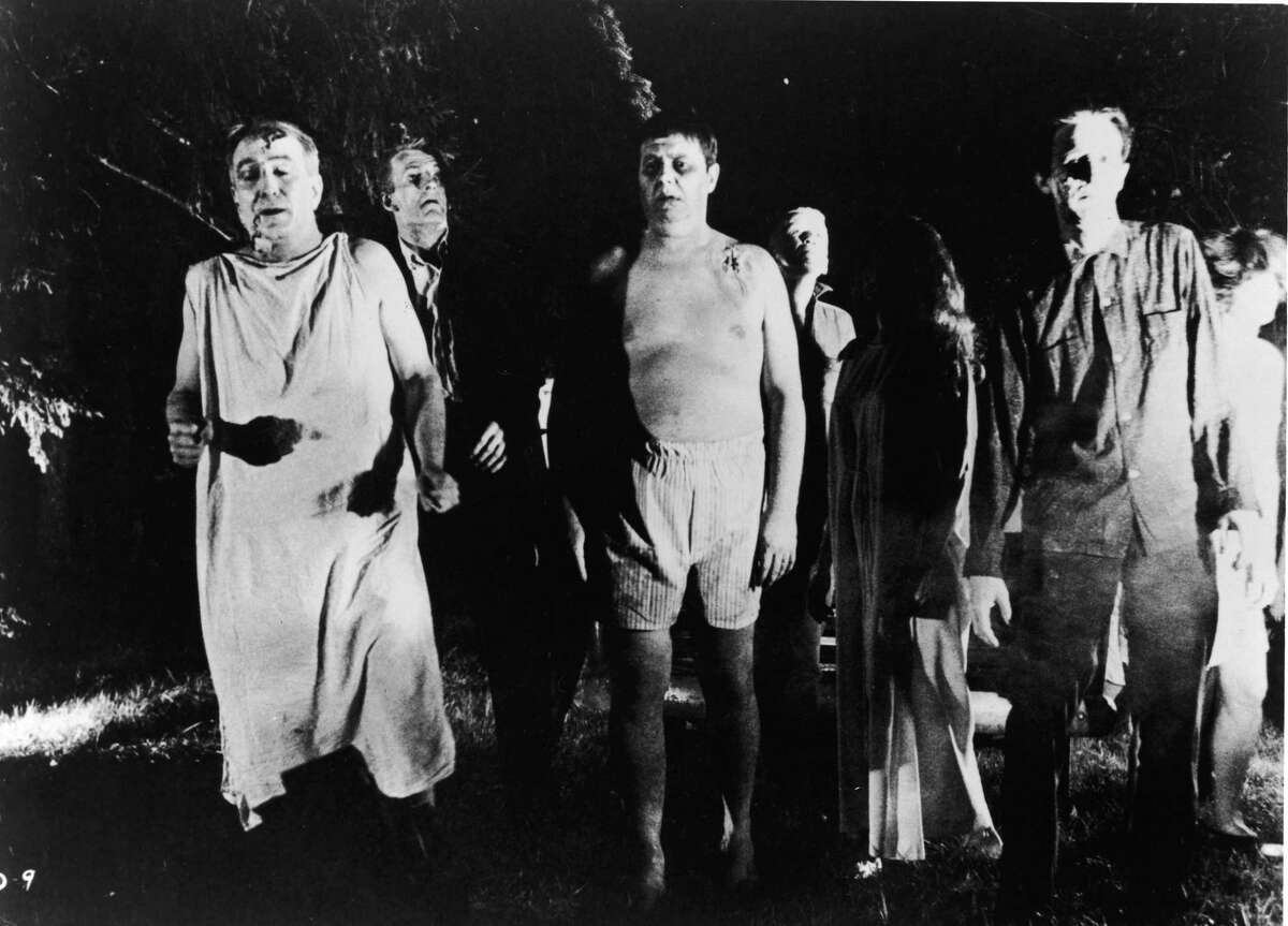 A line of undead “zombies” walk through a field in the film, “Night Of The Living Dead,” directed by George Romero.