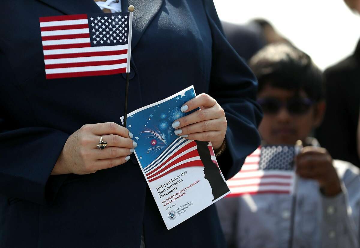FILE--  An immigrant holds an American flag before being sworn in as an American citizen during a naturalization ceremony on the flight deck of the USS Hornet on July 3, 2018 in Alameda. A federal judge upheld the core of California’s sanctuary laws Thursday, rejecting a Trump administration lawsuit that argued the state was violating U.S. law by restricting local cooperation with federal immigration agents.