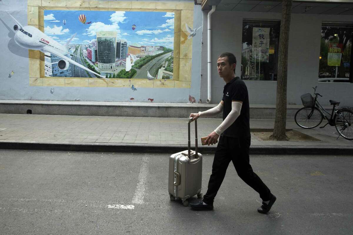 A man pushes a piece of luggage past a mural depicting air travel and a prosperous city in Beijing, China, Tuesday, July 3, 2018. Barring a last-minute breakthrough, the Trump administration on Friday will start imposing tariffs on $34 billion in Chinese imports. And China will promptly strike back with tariffs on an equal amount of U.S. exports.