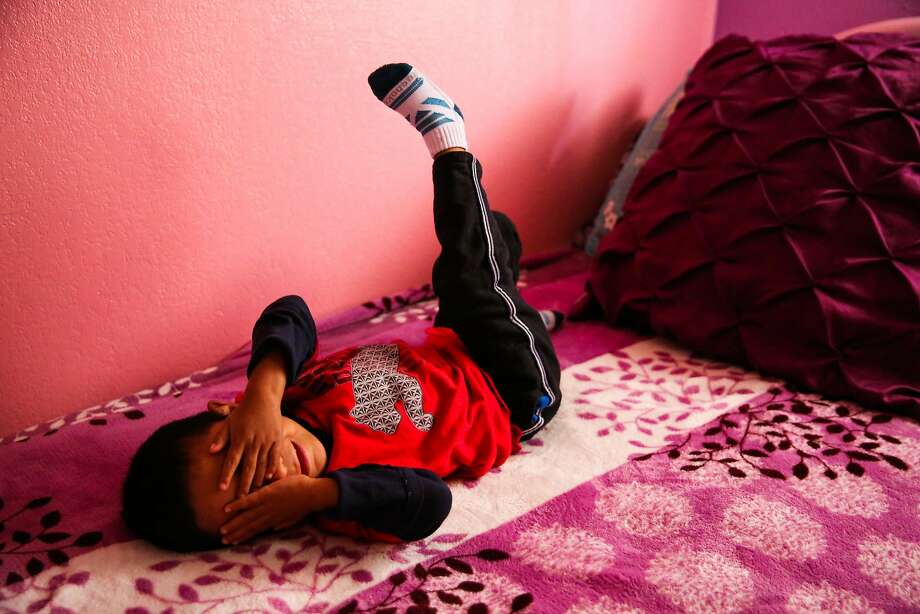 Jorgito, 5, covers his face for a portrait as he lays on a bed in the apartment he is staying in with his cousins in San Mateo, California, on Thursday, July 5, 2018. Jorgito was separated from his mother at the Texas border and she was since deported back to Guatemala. He is being cared for by his cousin Margarita. Photo: Gabrielle Lurie / The Chronicle