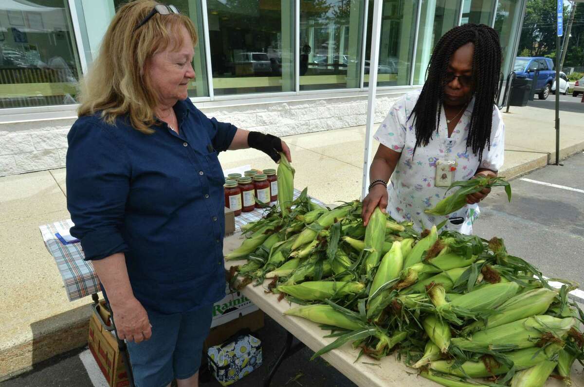 Lyn Detroy, Market Master for the City of Norwalk's farmers markets helps Manette Destin choose some corn on the cob at the JC Farm and Greenhouses Farmers Market at The Norwalk Community Health Center on Wednesday July 11, 2018 in Norwalk Conn.