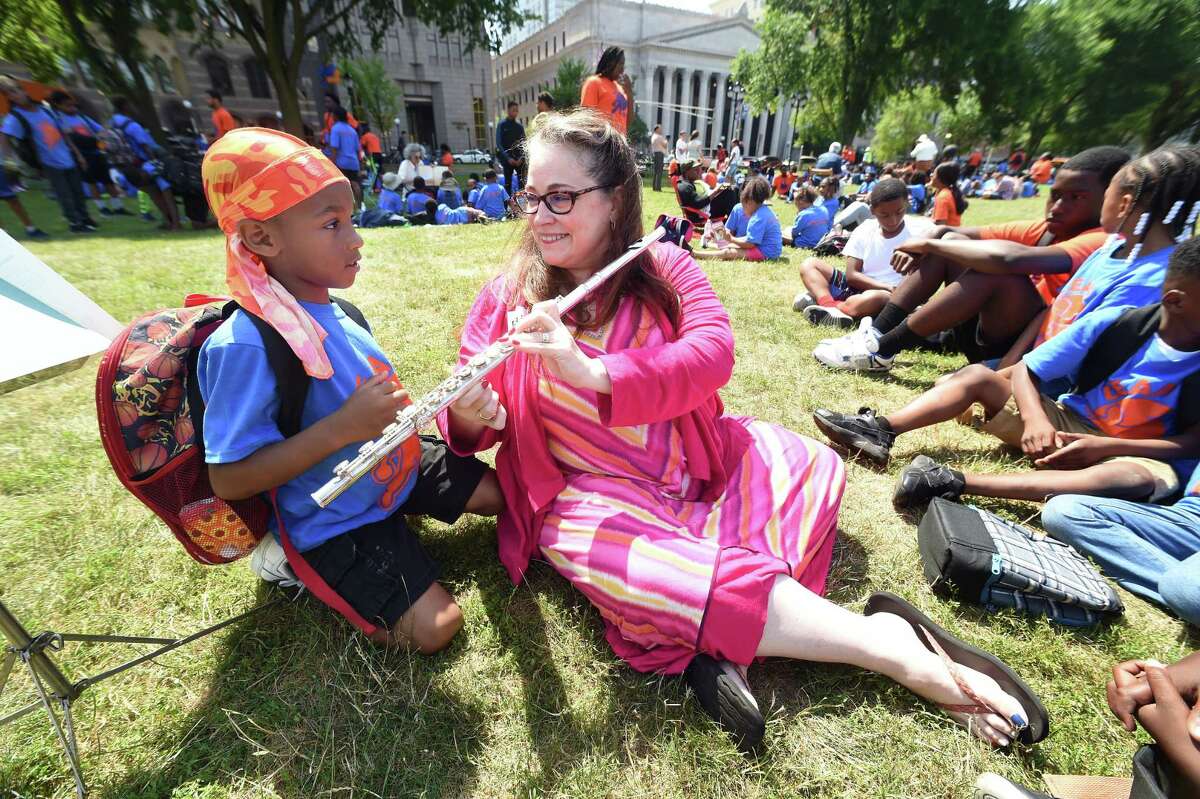 Tramire Miller, left, 7, controls the keys of the flute while New Haven Symphony CEO Elaine Carroll plays the instrument after reading “The Flute Player” during the LEAP Read-In on the Green in New Haven Friday.