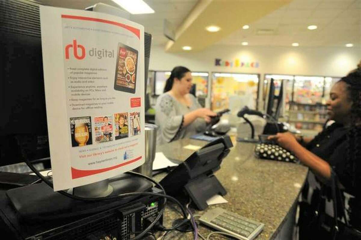 Hayner Public Library assistant Morgan Berry (left) helps patron Sheikera Balentine of Godfrey check items out on Sunday at the library’s Alton Square Mall branch. A flier advertising the library’s new digital offerings can be seen in the foreground.