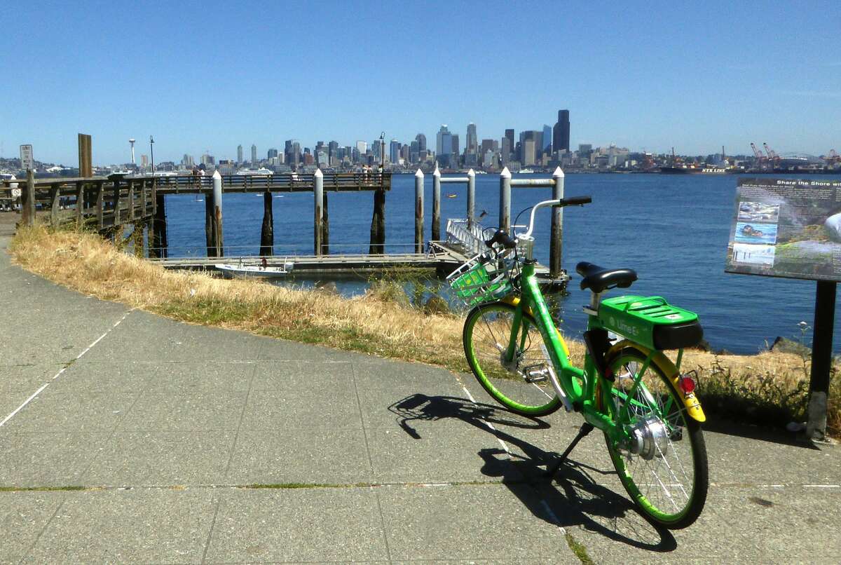 An electric LimeBike parked near the water with downtown Seattle in the distance.
