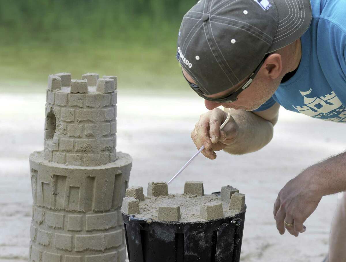 Kevin Lane, of New Milford, uses a straw to blow excess sand from his sculpture June 22, at Lynn Deming Park in New Milford. Lane and his family invented a system for building sandcastles and snow sculptures.