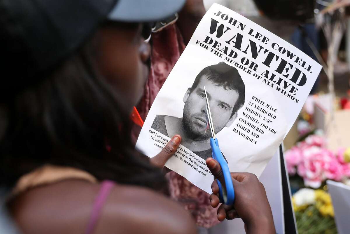 A young woman, who didn't want to be identified, cuts a wanted poster of John Lee Cowell during a vigil in memory of stabbing victim Nia Wilson at McArthur BART Station in Oakland, Calif. on Monday, July 23, 2018.