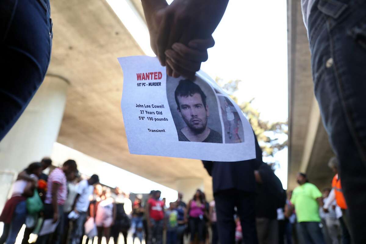 Two people hold a wanted poster for John Lee Cowell during a prayer circle at a vigil in memory of stabbing victim Nia Wilson at McArthur BART Station in Oakland, Calif. on Monday, July 23, 2018.