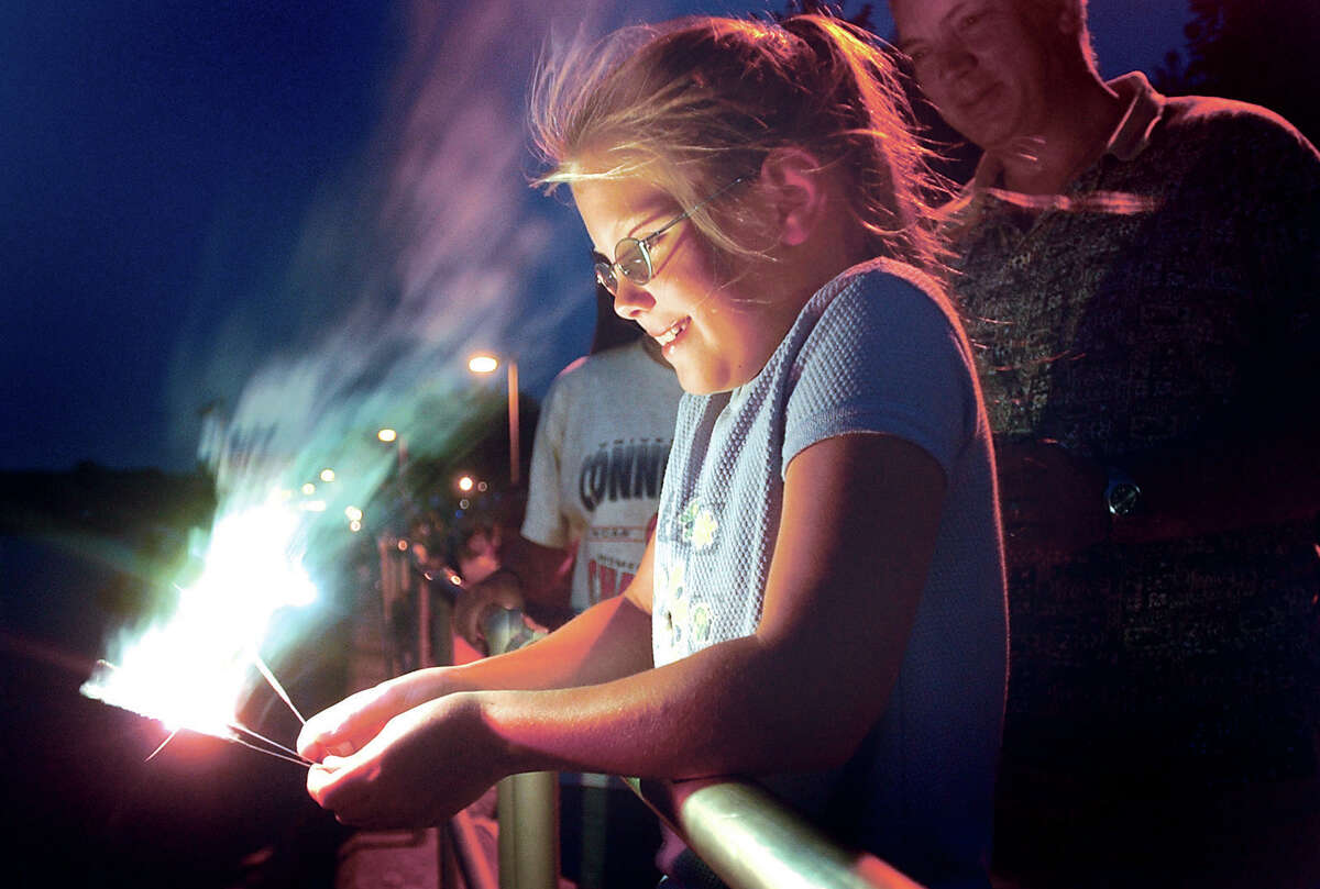 Julia Messier, 8, of Cromwell holds sparklers over the rail beside the Connecticut River Sunday as her father, Paul, stands behind her at Harbor Park in Middletown while waiting for the fireworks display to begin. 