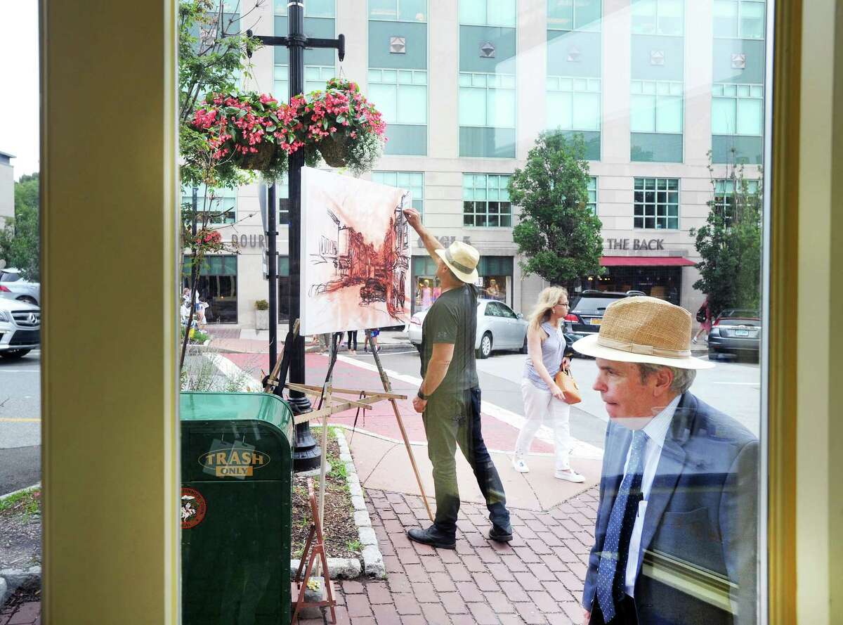 During a break from the rainy weather, Newtown artist Jim Chillington draws a Greenwich Avenue scene at the corner of Grigg Street just outside the Meli-Melo Creperie in Greewich, Conn., Wednesday, July 25, 2018. At right walking north on Greenwich Avenue is Greenwich resident Carl Carlson. 