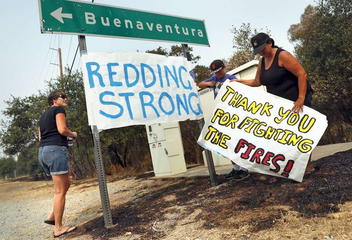 Redding residents Julie Reaves (left), Aiden Bunas, 11, and Naomi Yamamoto put up homemade signs along Eureka Way in the aftermath of the Carr Fire in Redding.