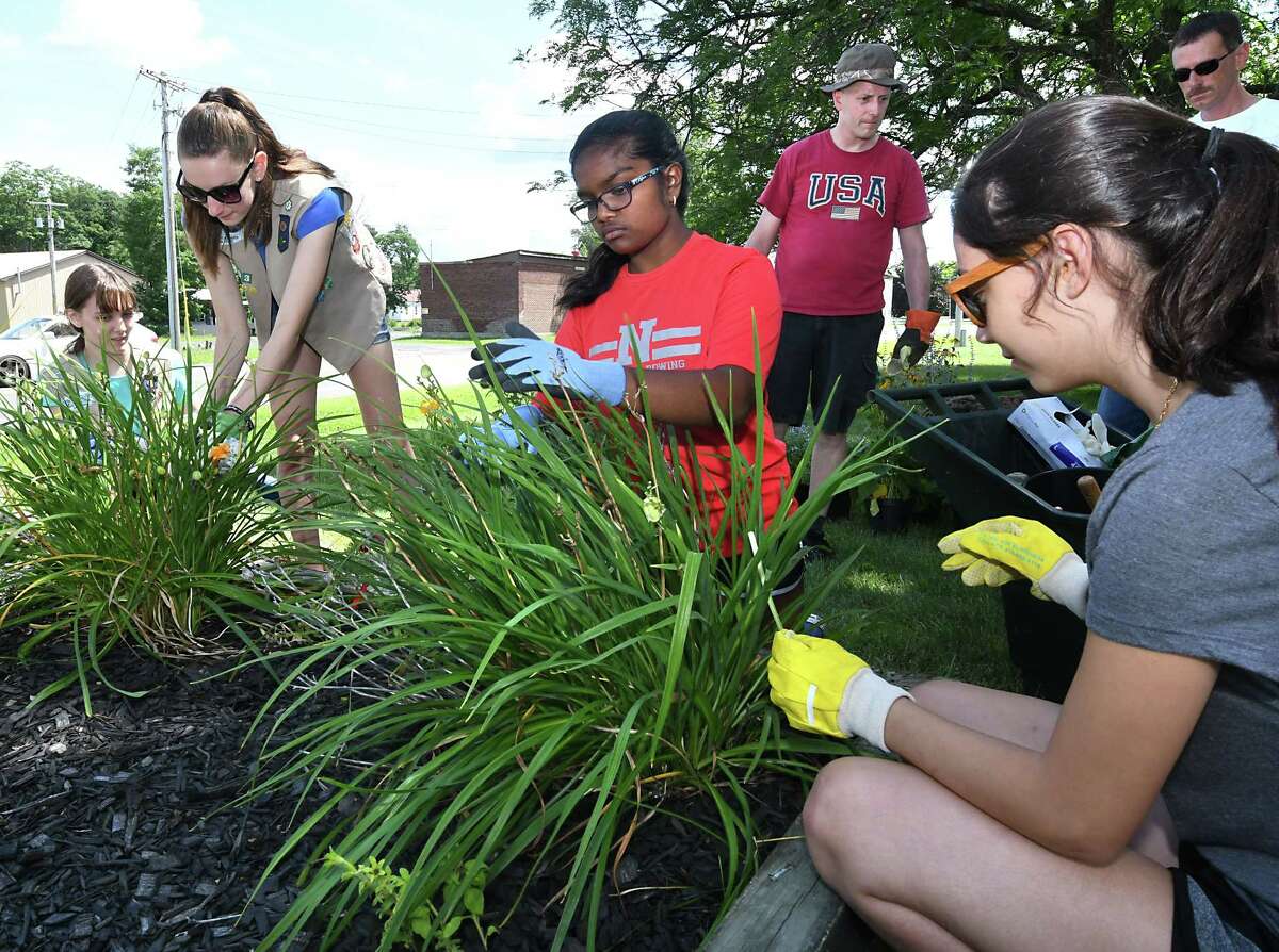 From left, Girl Scouts Kira Streichert, 14, Kathryn Braun,14, and volunteers Jessica Arul, 14, and Lisandra O'Hea, 13, help plant flowers around the entranceway sign for the Albany County Nursing Home on Sunday, July 29, 2018 in Albany, N.Y. The Guilderland Girl Scout Troop 1003 are doing community work to earn their Silver Award. Art Grimshaw, third from right, and Patrick Braun, right, helped out. (Lori Van Buren/Times Union)