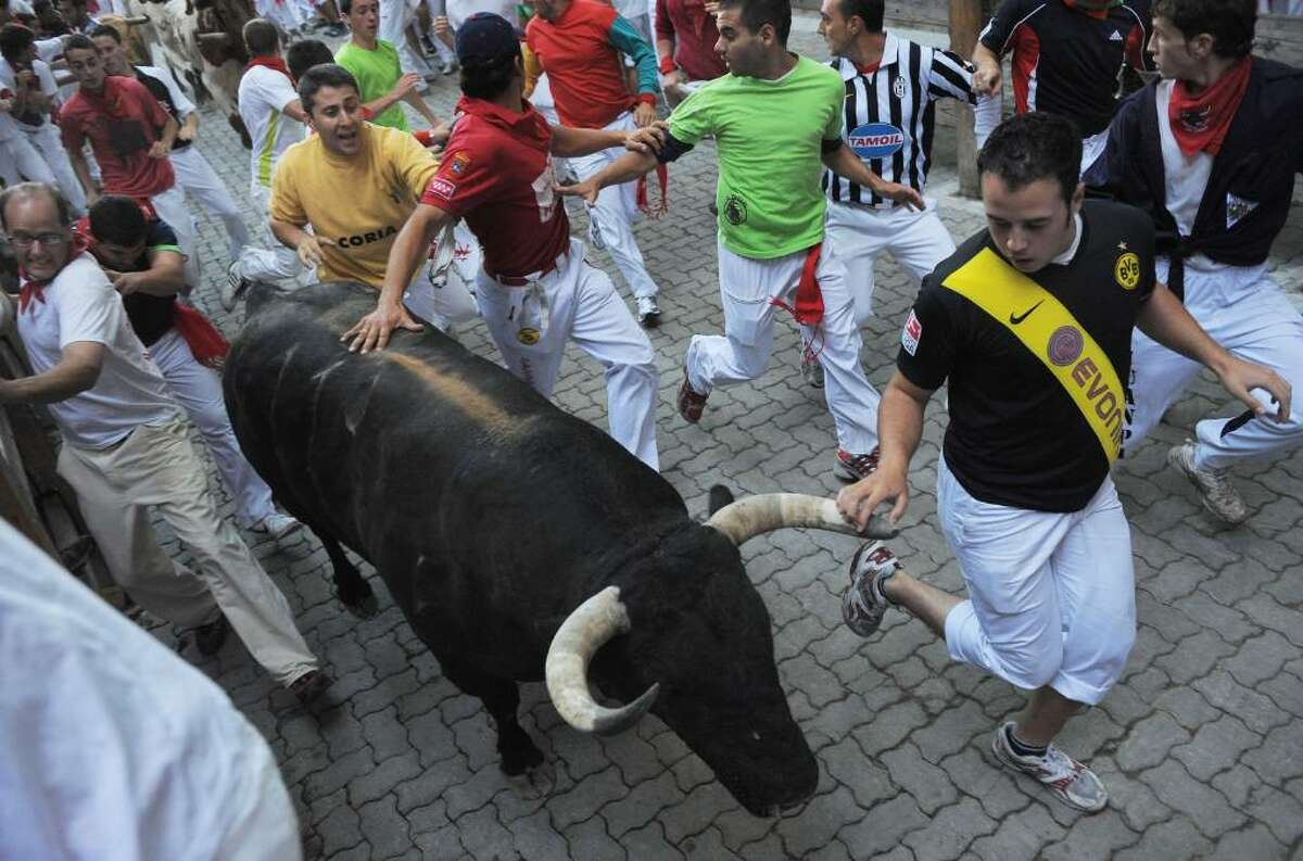 PAMPLONA, SPAIN - JULY 08: People run beside a fighting bull during the second bullrun of the San Fermin fiesta on July 8, 2010 in Pamplona, Spain. Fighting bulls run through the historic heart of Pamplona for eight days in this fiesta made famous by the 1926 novel of U.S. writer Ernest Hemmingway called 'The Sun Also Rises'. > on July 8, 2010 in Pamplona, Spain. (Photo by Denis Doyle/Getty Images)