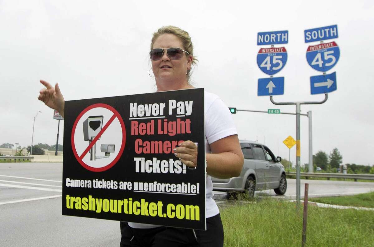 Kelli Cook waves to motorists as she and others protest red-light cameras on the corner of FM 1097 and Interstate 45 on Aug. 8, 2017, in Willis.