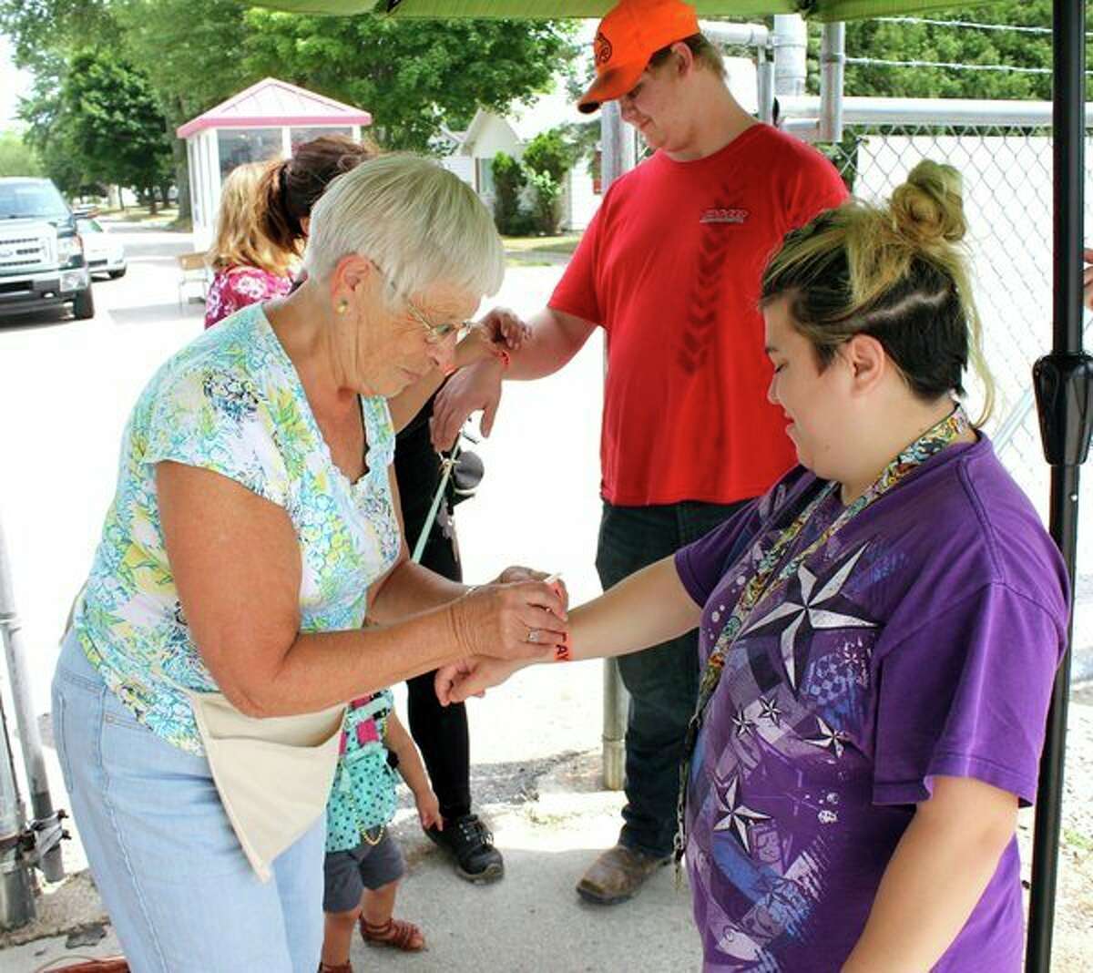 Joann Cove, left, helps Nicole Duda with her admission bracelet to the Huron Community Fair. Cove has worked the gate for 25 years. Also pictured is Cody Koglin. (Brenda Battel/Huron Daily Tribune)