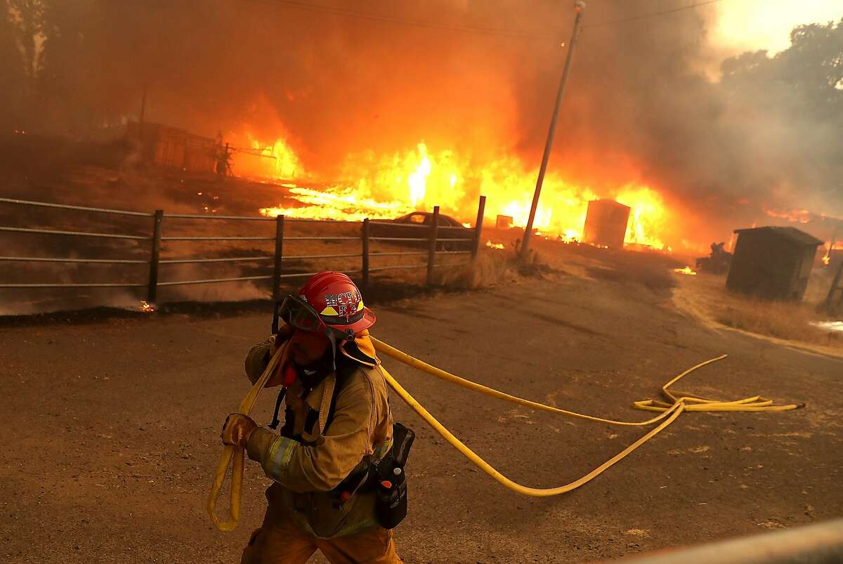 A West Covina firefighter pulls hose away from a barn as the River Fire goes through Lake County.