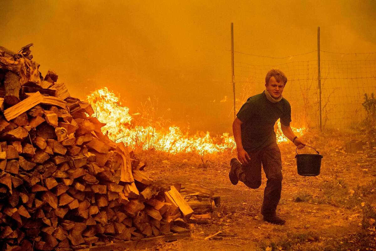 TOPSHOT - Alex Schenck carries a water bucket while fighting to save his home as the Ranch Fire tears down New Long Valley Rd near Clearlake Oaks, California, on Saturday, August 4, 2018. The Ranch Fire is part of the Mendocino Complex, which is made up of two blazes, the River Fire and the Ranch Fire. / AFP PHOTO / NOAH BERGERNOAH BERGER/AFP/Getty Images