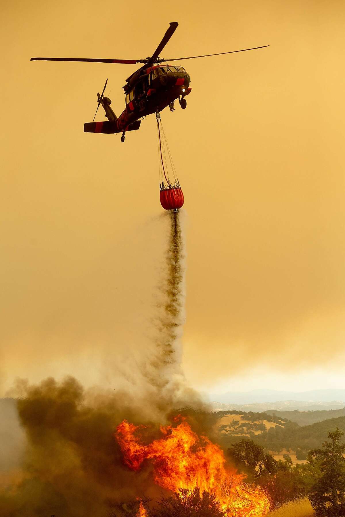 A helicopter drops water on the Ranch Fire, part of the Mendocino Complex Fire, burning on High Valley Rd. near Clearlake Oaks, California, on Sunday, Aug. 5, 2018. / AFP PHOTO / NOAH BERGERNOAH BERGER/AFP/Getty Images