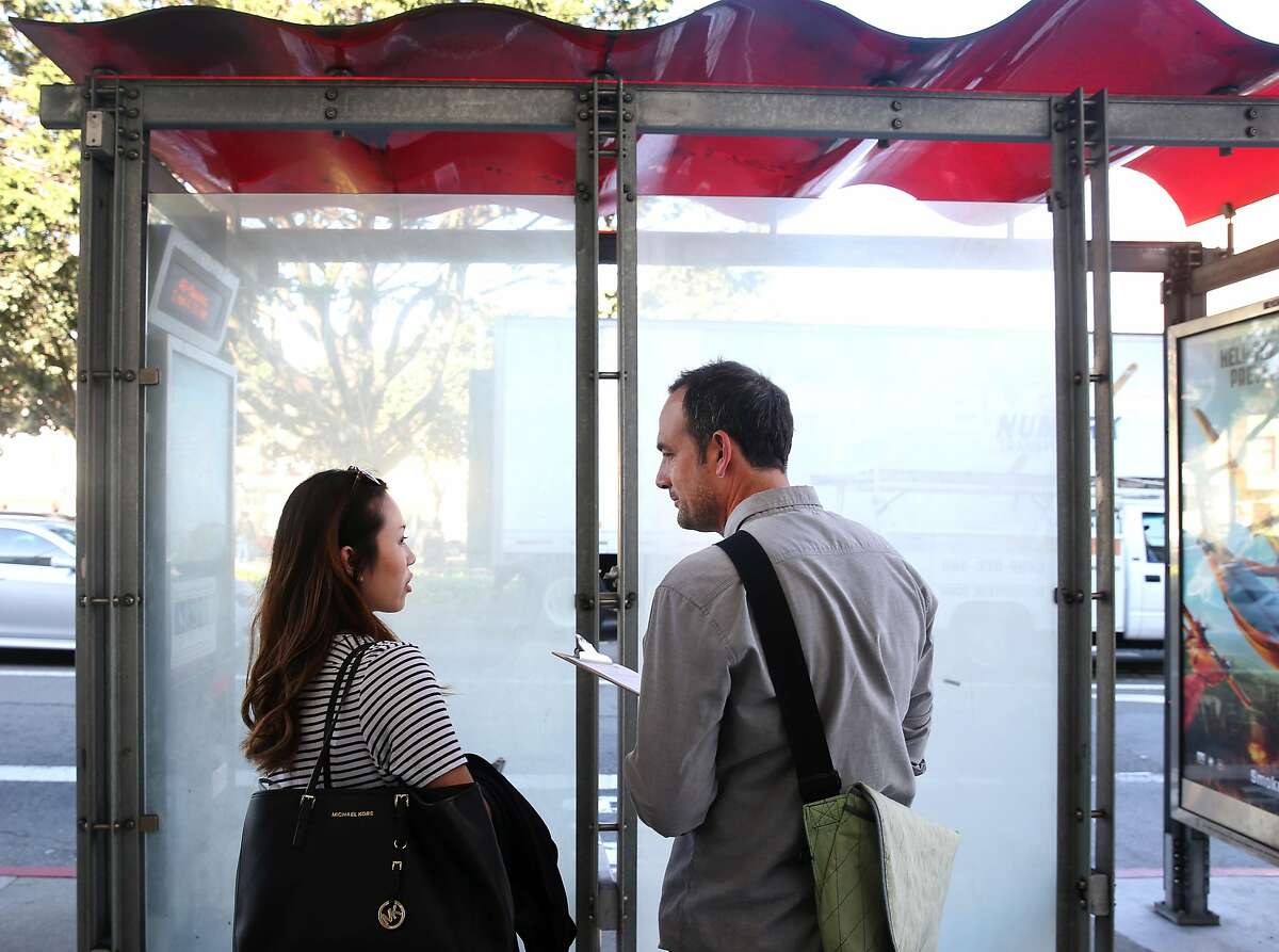 Artist Scott Oliver (right) interviews a commuter, who said her name is Emily, while she waits at a bus stop on Masonic Avenue and Geary Boulevard in San Francisco, Calif. on Thursday, March 12, 2015. "Points of Departure", a public art project created by Oliver, has been chosen for the site when major renovation of the area is completed by the Department of Public Works.