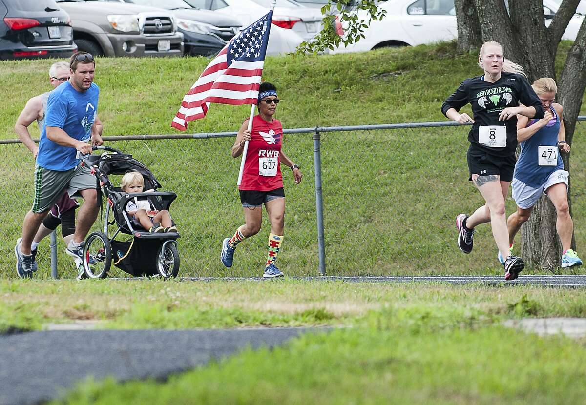 Sarah Greaney, of Lewiston, Maine carries the American flag Sunday July 22, 2018, as she heads into the home stretch of Emily's Run that started and finished at Edward Little High School in Auburn, Maine. She has no military background but is a member of Team Red White and Blue, a national service organization that brings physical fitness challenges and fun social activities to veterans combating PTSD. The race, in it's 14th year is run in honor of Emily Fletcher, a local runner killed in an automobile accident in 2004. (Russ Dillingham/Sun Journal via AP)
