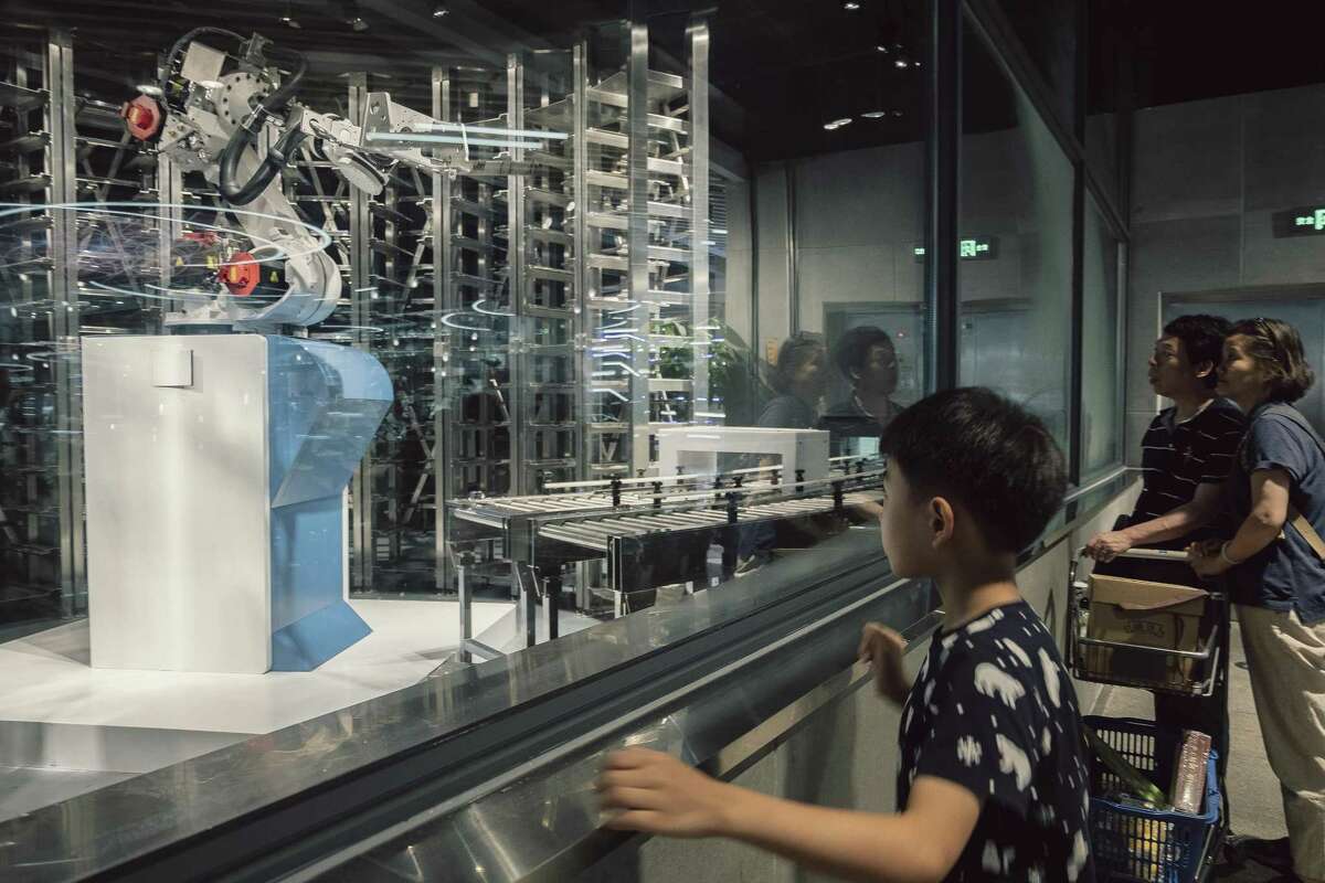 Customers watch robots take cooked food out onto a sort of runway that connects the kitchen to the seating area at the Alibaba-owned Hema grocery store in Shanghai, June 27, 2018. China has embraced technology full tilt, no matter how questionable. (Yuyang Liu/The New York Times)