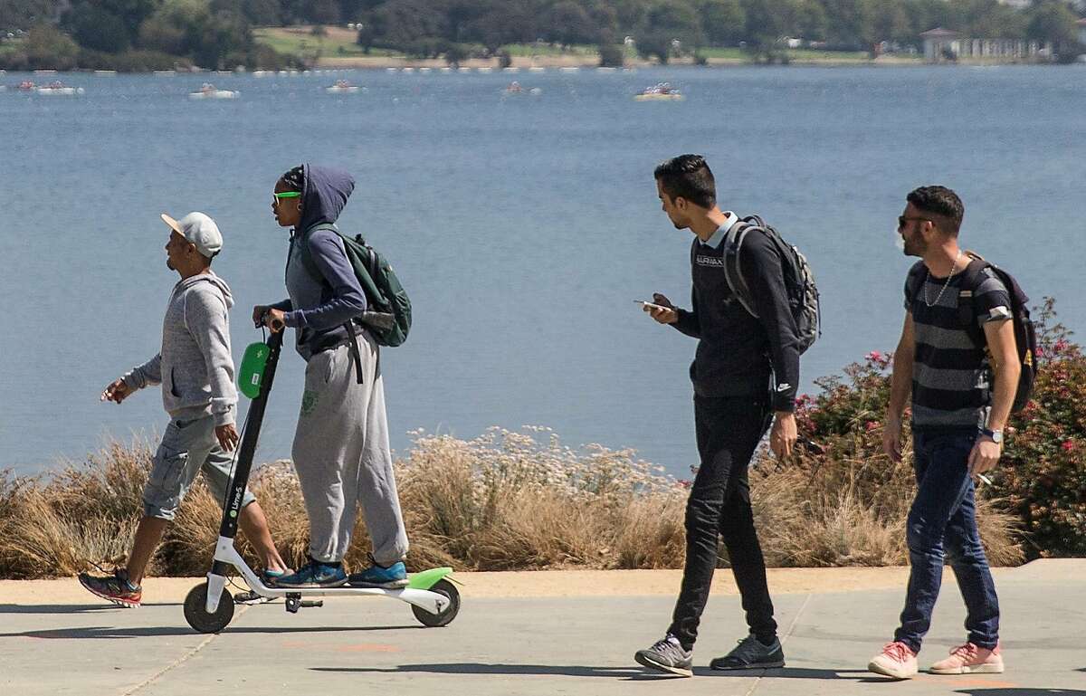 A woman rides a Lime electronic scooter around Lake Merritt in Oakland, Calif. Thursday, Aug. 16, 2018.