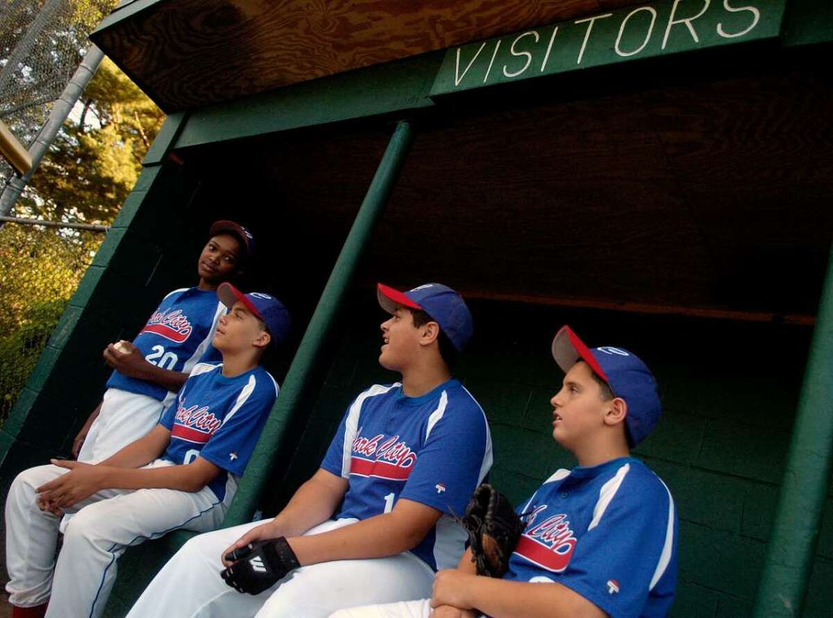 A young, black baseball player sits in the dugout during a