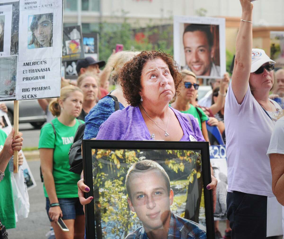 Nancy Tobin, of Hudson, Mass., looks skyward as she holds a poster photo of her late son, Scott Tobin, who died in 2017 and who she said was a victim of the opioid crisis, during a protest against Purdue Pharma, the maker of the opioid OxyContin, outside Purdue Pharma's headquarters at 201 Tresser Blvd., in Stamford, Conn., on Friday, August 17, 2018. Protesters said OxyContin is highly addictive and can be directly blamed for the opioid-related deaths of their loved ones.