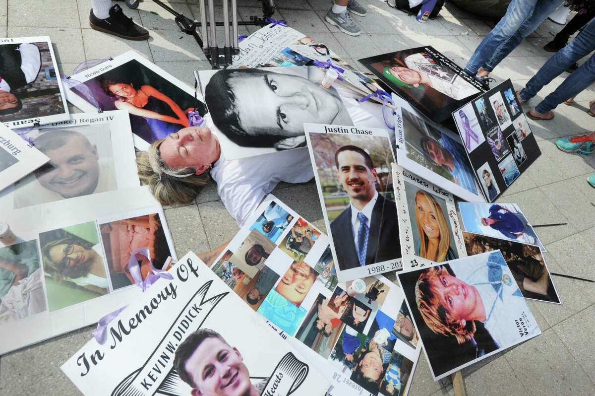 Joan Peters-Gilmartin, of Falmouth, Mass., lays down on the sidewalk surrounded by photos of victims of the opioid crisis, including her late son, Cory Gilmartin, who died in 2014 of a heroin overdose during a protest against OxyContin maker Purdue Pharma, outside the company’s headquarters at 201 Tresser Blvd., in downtown Stamford, Conn., on Friday, Aug. 17, 2018.