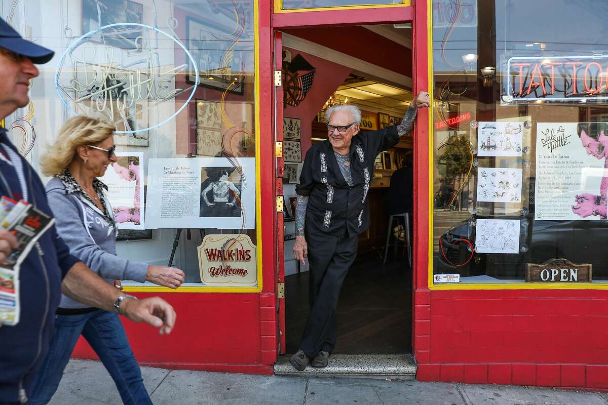 2018年8月14日，加利福尼亚州旧金山，莱尔·塔特尔在他的纹身店里摆姿势拍照，与路过的人打招呼。