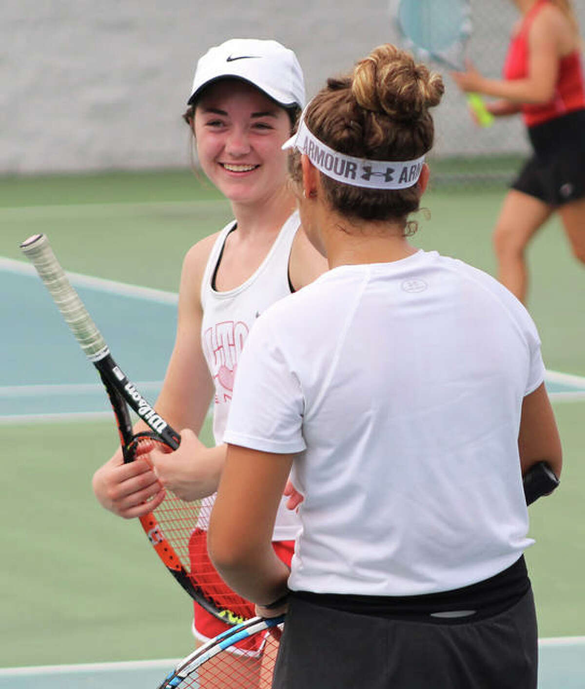 Alton’s Maddi Saenz (left) shares a laugh with doubles partner Hannah Macias between points in their victory over Bradley-Bourbonnais on Saturday at the LCCC’s Andy Simpson Tennis Complex in Godfrey.