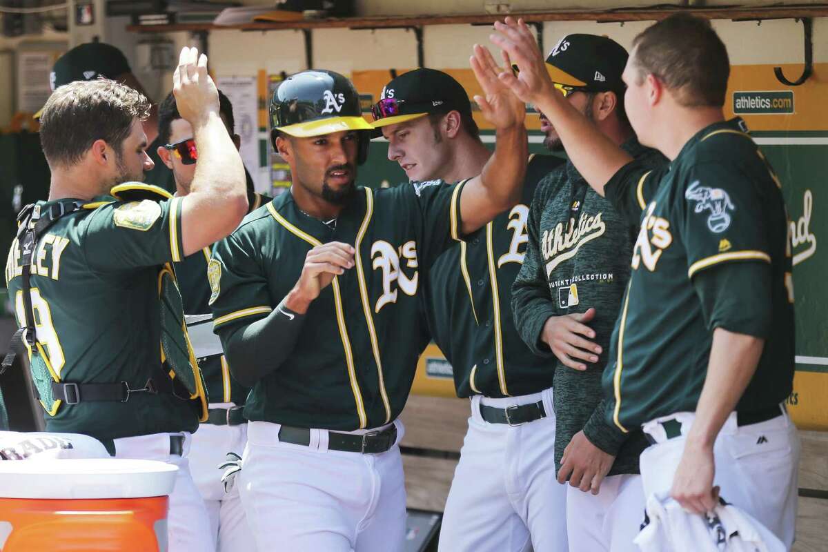 Oakland Athletics shortstop Marcus Semien (10) is greeted by teammates back at the dugout after scoring on a line drive by A's Khris Davis (2) during the first inning of an MLB game between the Oakland Athletics and Houston Astros at the Oakland-Alameda County Coliseum on Saturday, Aug. 18, 2018, in Oakland, Calif.