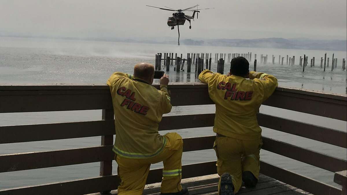 In Lucerne, South Santa Clara County Fire District Capt. Mark Treichel, left, and a strike team colleague videotape a helicopter sucking water out of Clear Lake to fight the Mendocino Complex fire. (Robin Abcarian / Los Angeles Times/TNS)