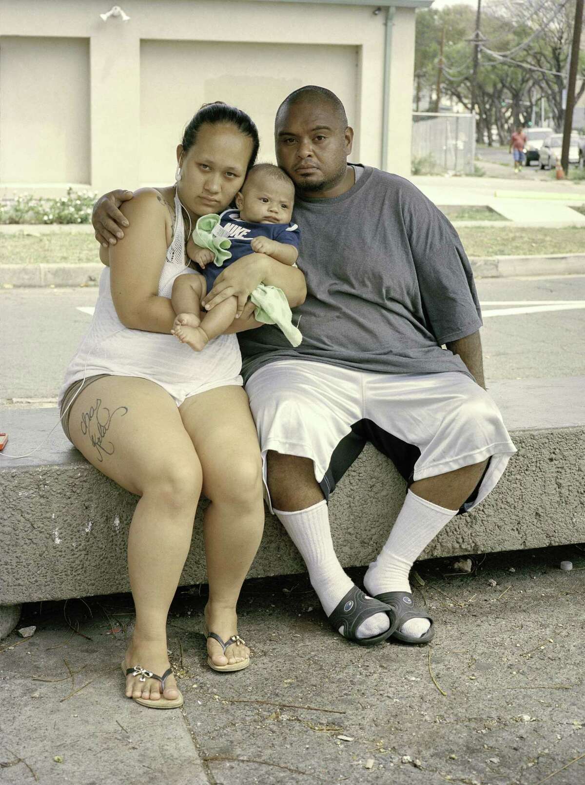 Chas, Kela and baby wait at a bus stop outside Micronesi Mart in Oahu, Hawaii.
