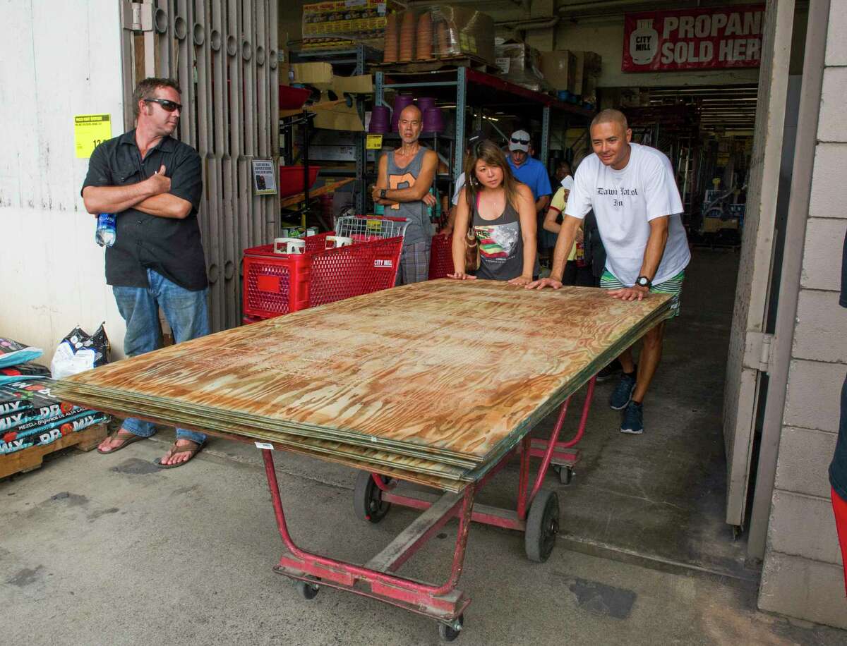 Jodi Nishida and Sam Delovio push along plywood they purchased at a City Mill store Tuesday, Aug. 21, 2018, before the arrival of Hurricane Lane in Hawaii. People hurried to buy water and other supplies and the Navy moved its ships to safety. (Craig T. Kojima/Honolulu Star-Advertiser via AP)